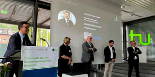 Professor Cadez steht am Rednerpult. Neben ihm vier Vortragende vor einer Leinwand.