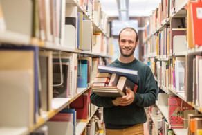 Student in Bibliothek Ein Student steht in der Bibliothek im Gang und hat Bücher auf dem Arm.